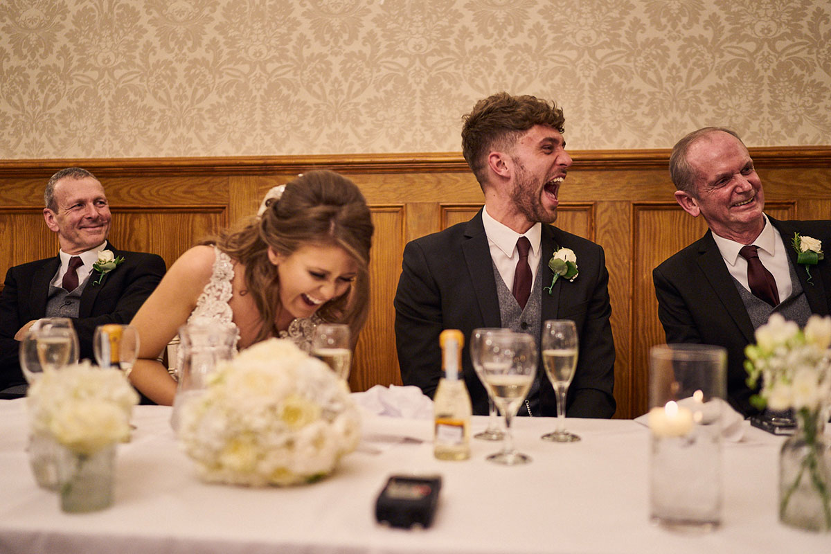 bride and groom laughing hard at wedding speeches